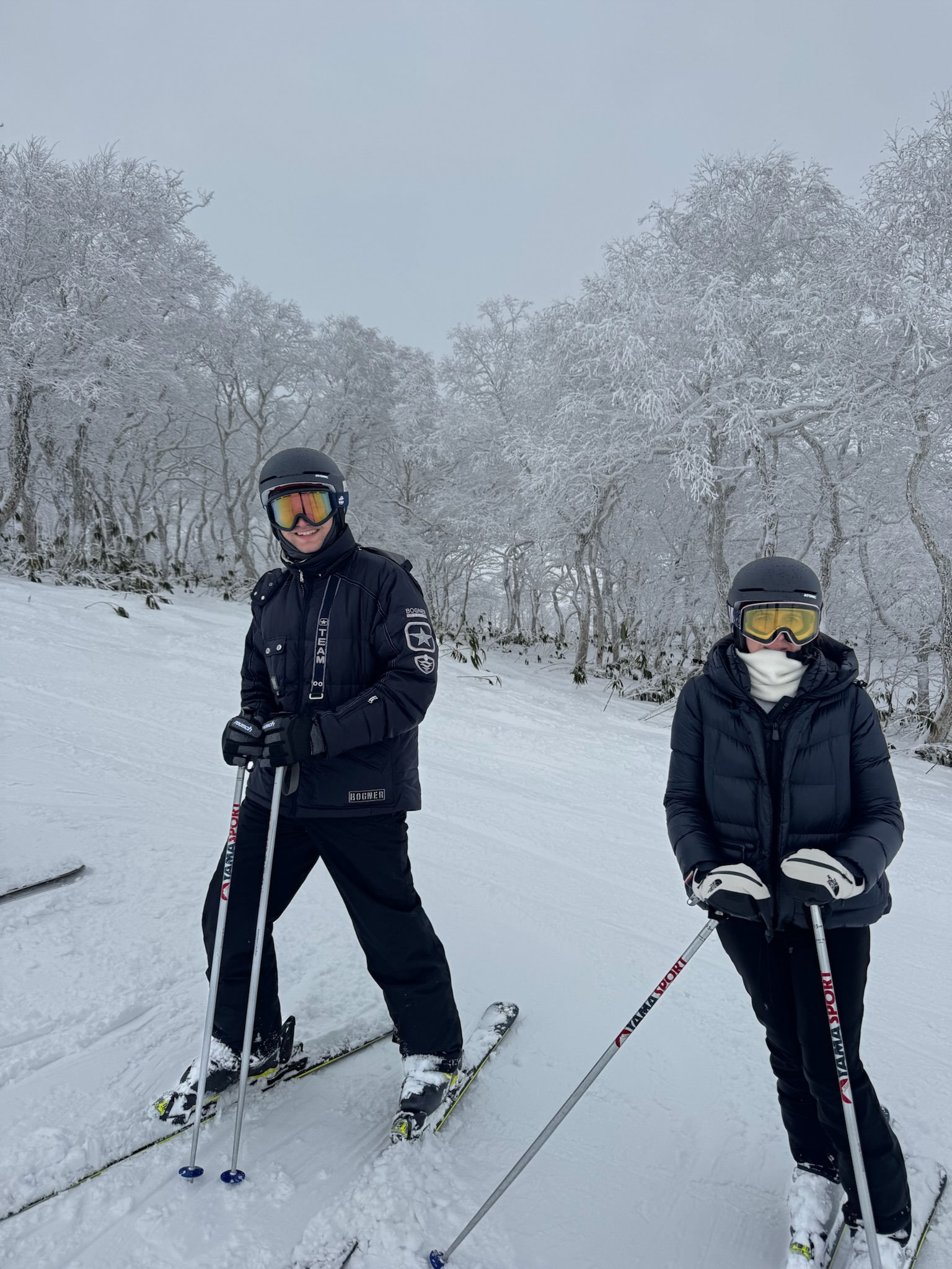 Two skiers standing on a snowy trail surrounded by snow-covered trees